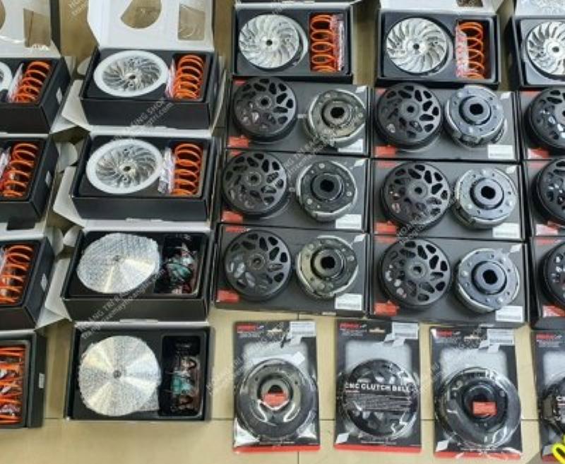 Bộ sưu tập các phụ kiện độ kiểng cho xe máy điện nhập khẩu bao gồm tay thắng CNC màu sắc, gương chiếu hậu thể thao, và van vòi lốp kiểu, đặt trên nền carbon fiber.
